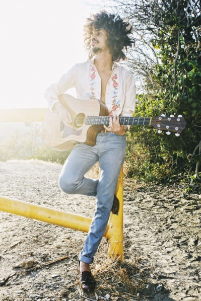 Mixed Race man leaning on gate playing guitar