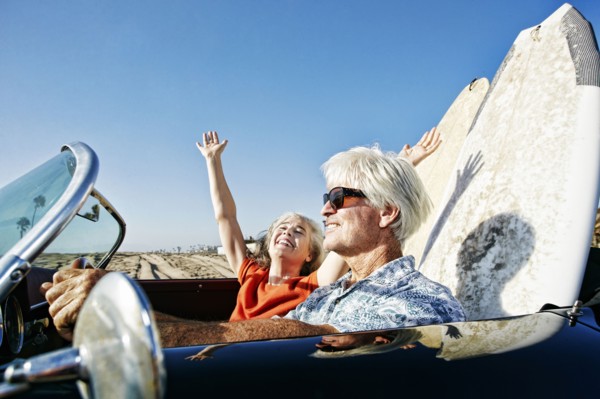 Older Caucasian couple in convertible car with surfboards on beach