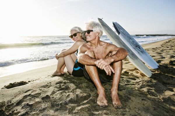 Older Caucasian couple sitting on beach with surfboards