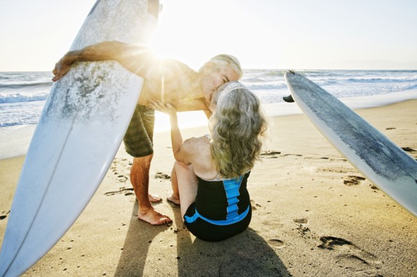 Older Caucasian couple on beach with surfboards kissing