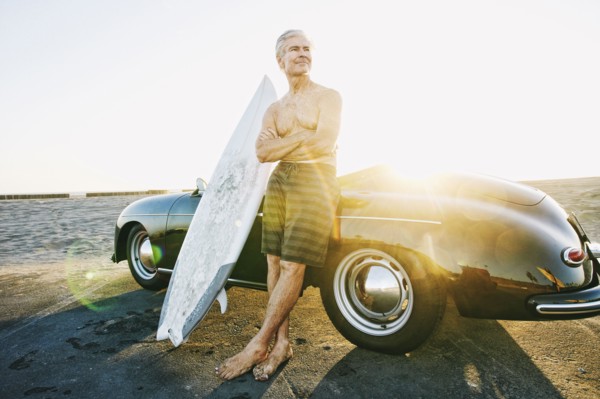 Older Caucasian man on leaning on convertible car with surfboard