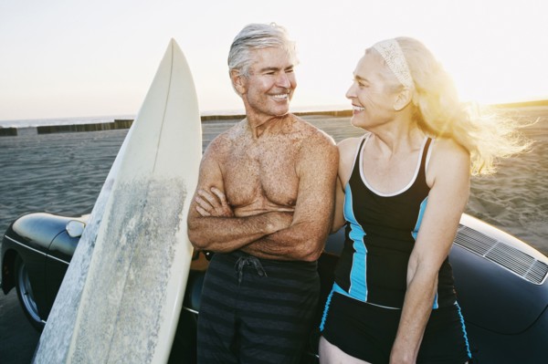 Older Caucasian couple leaning on convertible car with surfboards