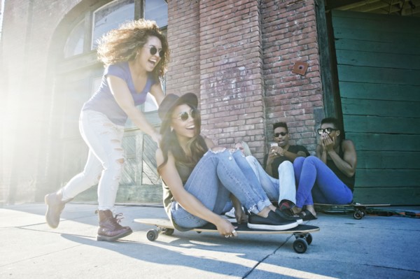 Woman pushing friend sitting on skateboard in city
