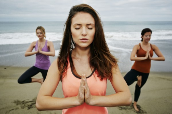 Caucasian women performing yoga on beach