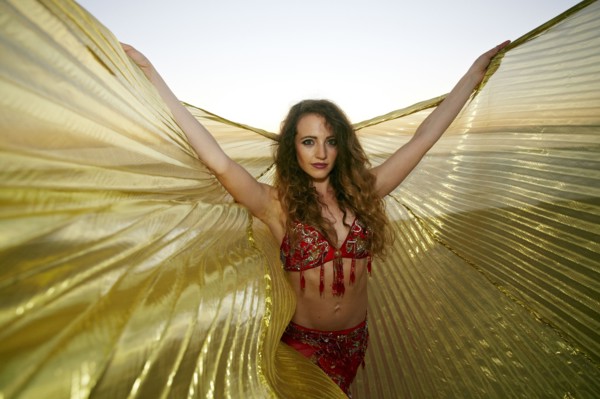 Caucasian belly dancer holding cape on beach