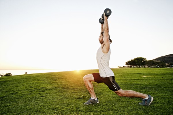 Caucasian man lifting dumbbells in sunny field