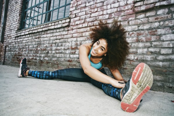 Hispanic woman sitting on sidewalk stretching legs near brick wall