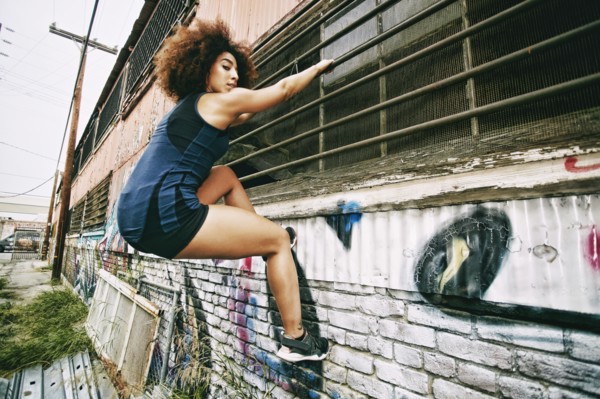 Hispanic woman climbing on bar on graffiti wall