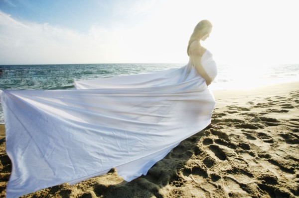 Wind blowing dress of Mixed Race expectant mother at beach