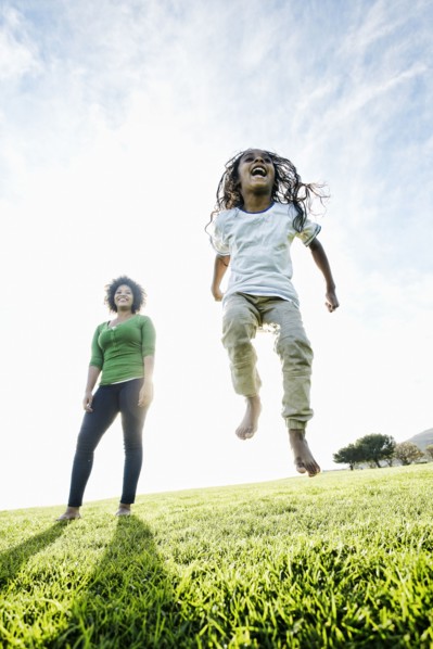 Mixed race mother watching daughter jumping in the grass