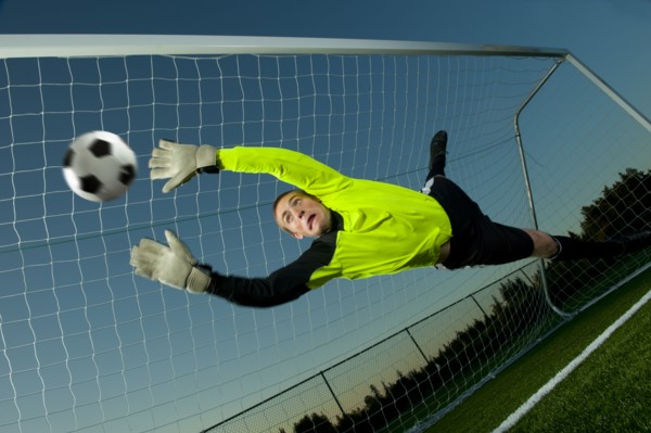 Caucasian goalie deflecting soccer ball
