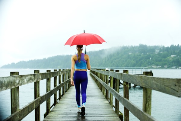 Caucasian woman in sportswear with red umbrella on pier