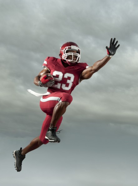 Black football player carrying football in mid-air