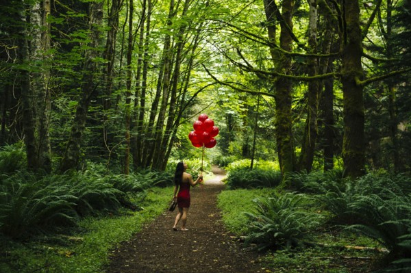 Korean woman holding red balloons in lush forest