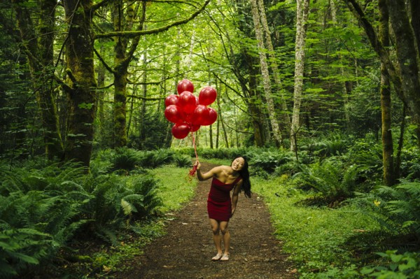 Korean woman holding red balloons in lush forest