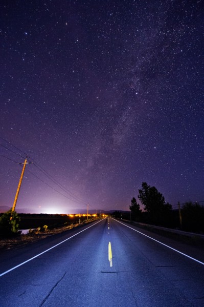Paved road under starry night sky illuminated by headlights
