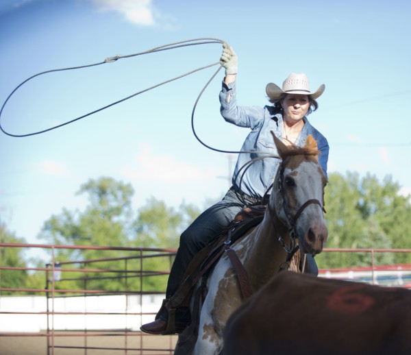 Caucasian cowgirl on horse throwing lasso on ranch