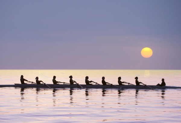 Silhouette of rowing team practicing on still lake