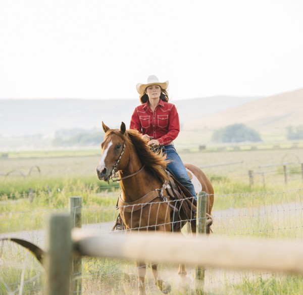 Caucasian cowgirl riding horse on ranch