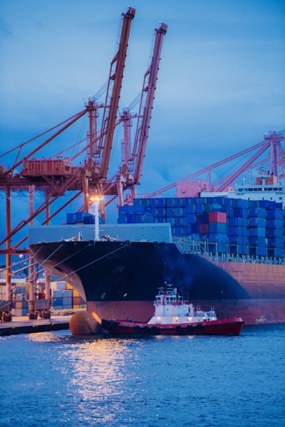 Cargo containers on freighter at shipping port near tugboat