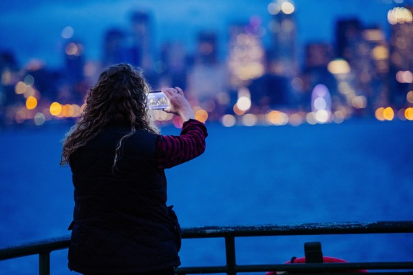 Caucasian woman on boat photographing urban waterfront with cell phone