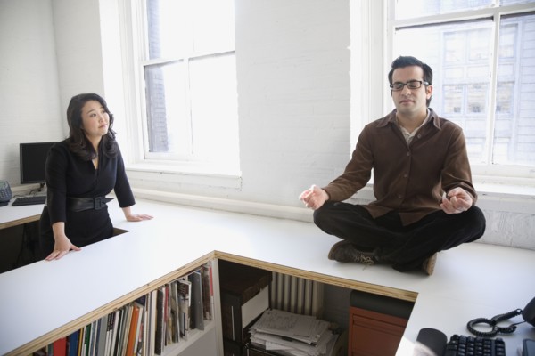 Hispanic businessman meditating next to coworker