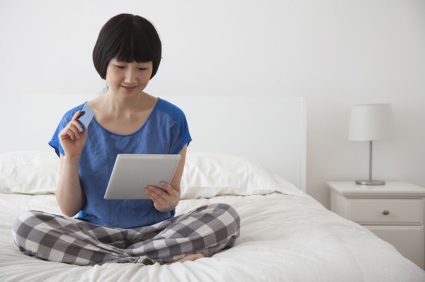 Chinese woman using tablet computer on bed