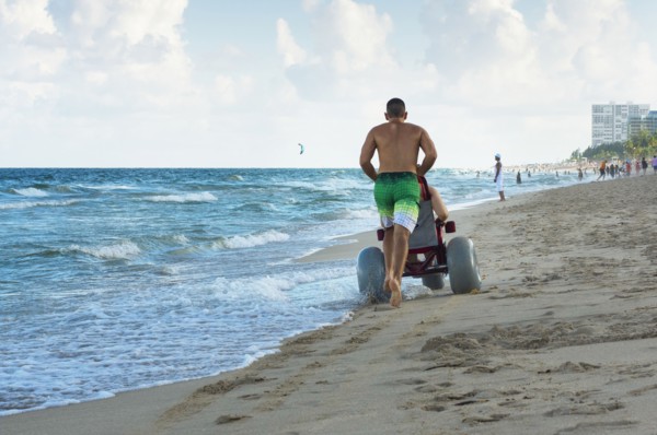 Man pushing paraplegic girlfriend in wheelchair on beach