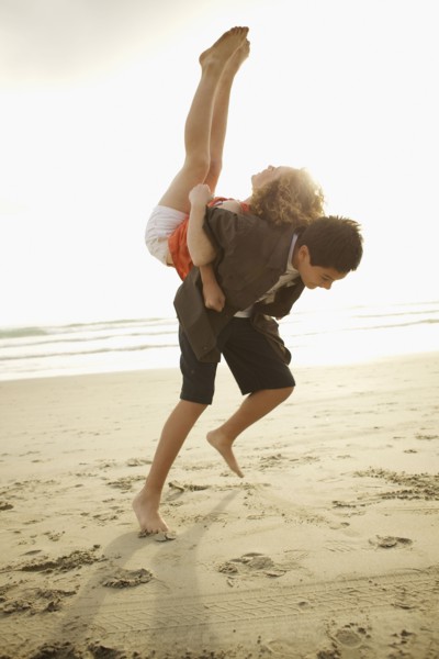 Boy lifting girl on back on beach