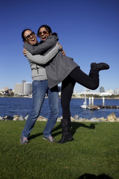 Grinning mixed race sisters hugging outdoors