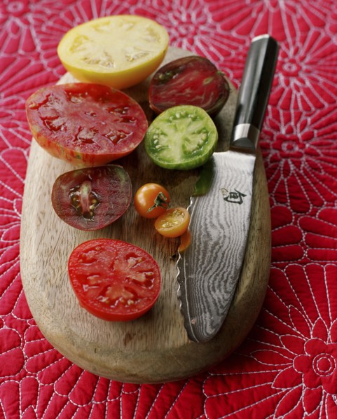 Various juicy sliced tomatoes on cutting board with knife