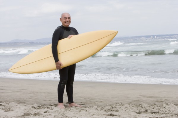 Senior Hispanic man holding surfboard on beach