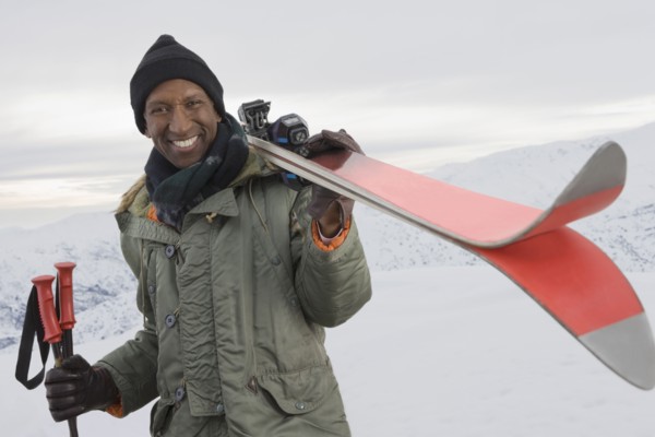 Mixed race man carrying skis on snowy slope