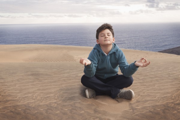 Hispanic boy meditating on sand dune over ocean