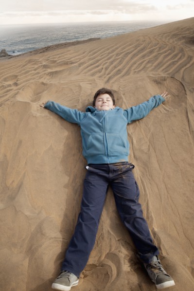 Hispanic boy laying on sand dune at beach