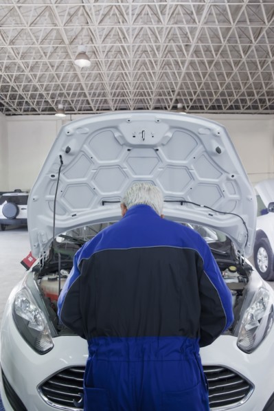 Older Hispanic mechanic repairing car in garage