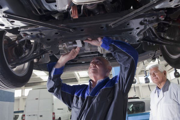 Older Hispanic mechanic repairing car in garage