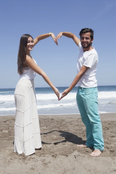 Hispanic couple forming heart-shape with arms at beach