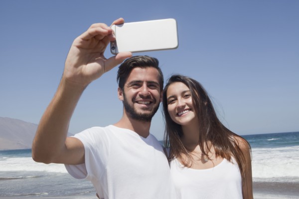 Hispanic couple posing for cell phone selfie at beach