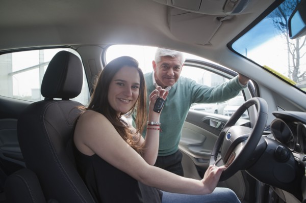 Hispanic woman sitting in new car showing key