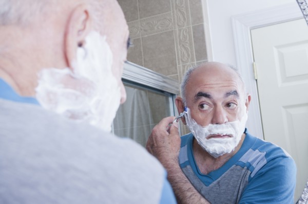 Reflection of Hispanic man shaving face in mirror
