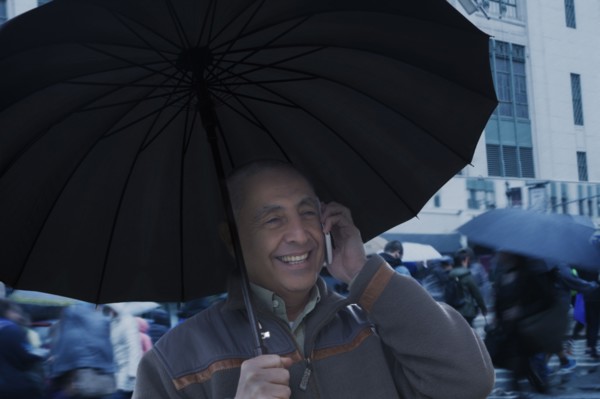 Smiling Hispanic man holding umbrella and talking on cell phone