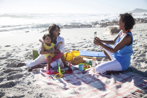 Mixed race mother photographing grandmother and daughter at beach