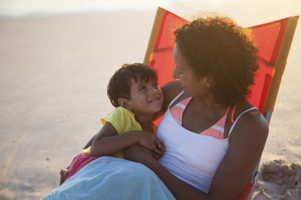 Mixed race mother and daughter hugging in chair on beach