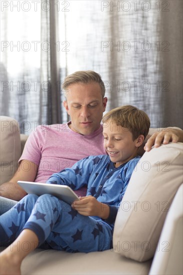 Caucasian father and son using digital tablet on sofa