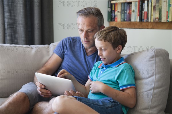Caucasian father and son using digital tablet on sofa
