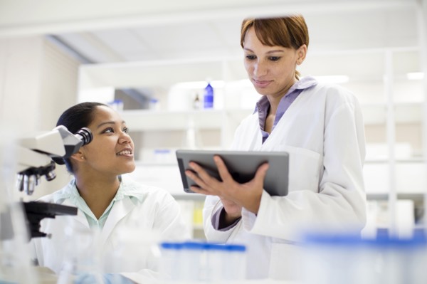 Scientists using digital tablet and microscope in laboratory