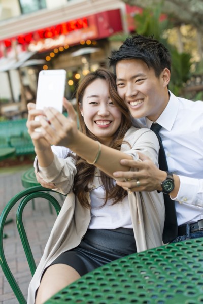 Korean couple taking cell phone photograph at sidewalk cafe