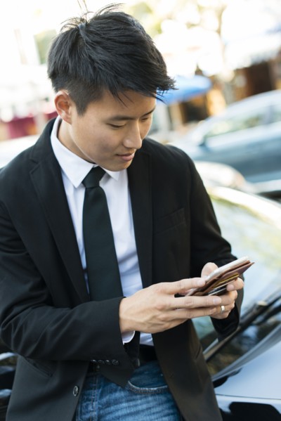 Korean businessman using cell phone near car