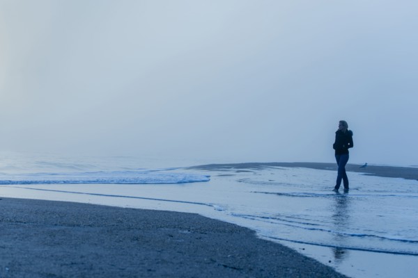 Caucasian woman walking in waves on beach